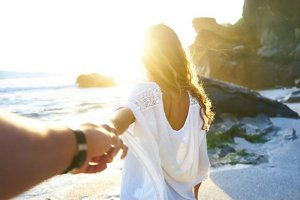 Woman reaching out to hold someone's hand as she walks along the beach at sunset